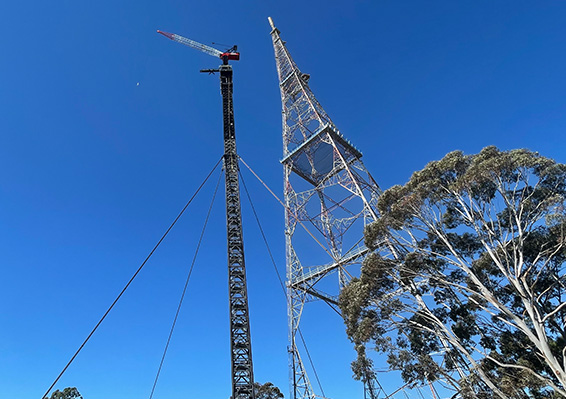 Tall communication tower with antenna and cables against blue sky with trees