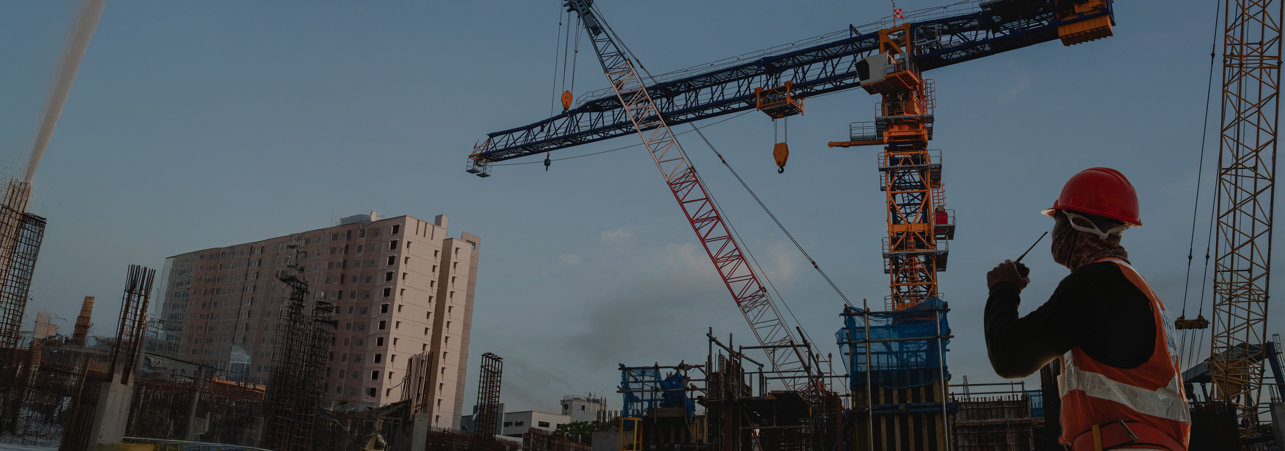 Construction site worker with communication equipment and crane overhead - desktop hero banner